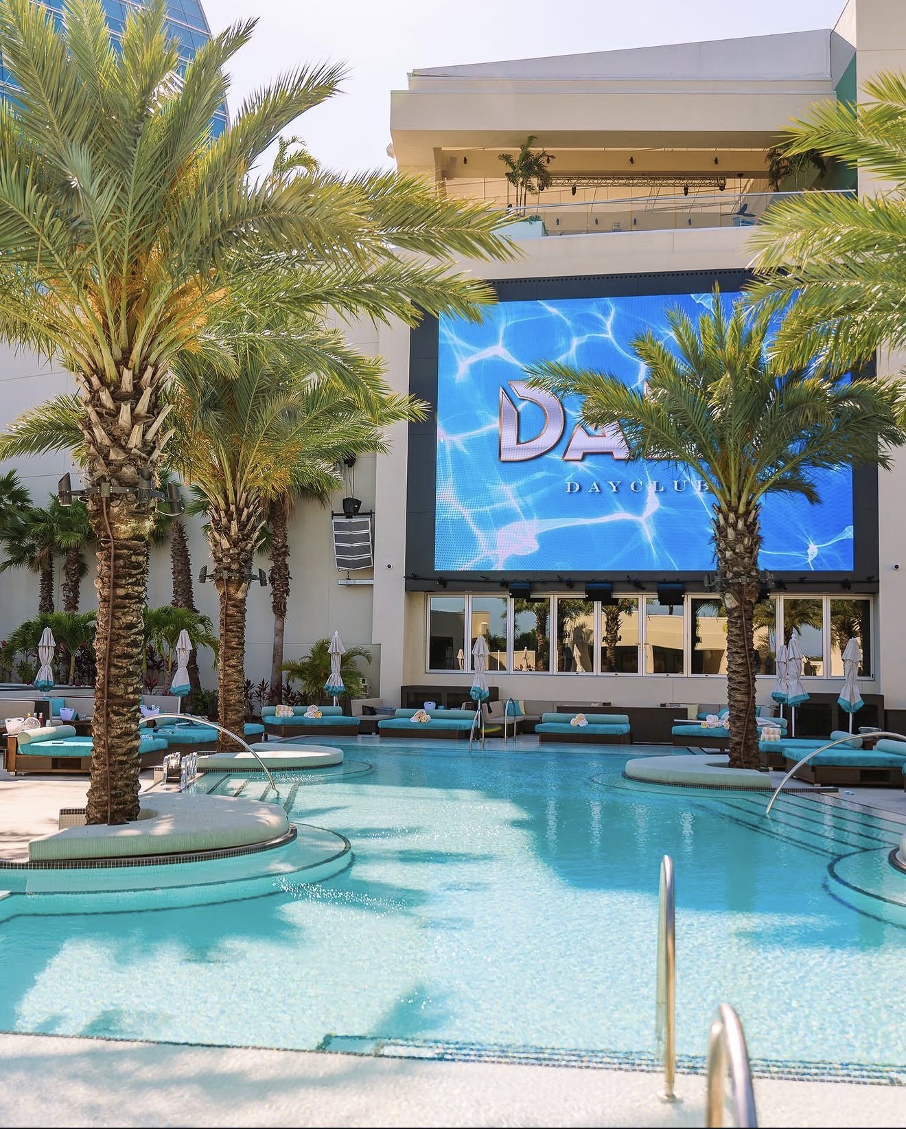 Daer Dayclub pool teal lounge chairs palm trees giant LED screen fountain jets
